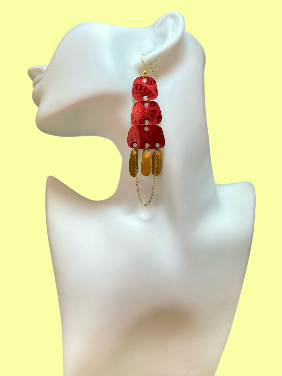 Golden red large earrings made from upcycled nespresso capsules on a white earrings display and yellow background