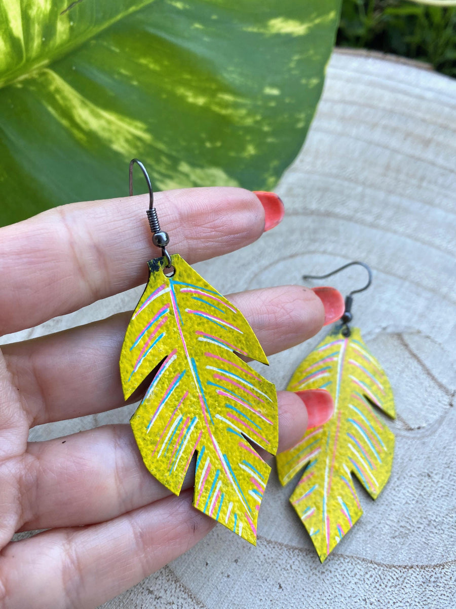 yellow coloured upcycled bicycle inner tube, tyre rubber earrings on a wooden background and a green  leaf