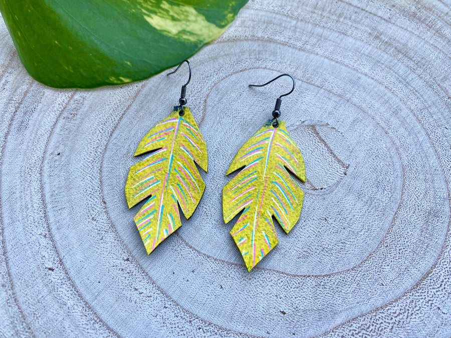 yellow coloured upcycled bicycle inner tube, tyre rubber earrings on a wooden background and a green  leaf