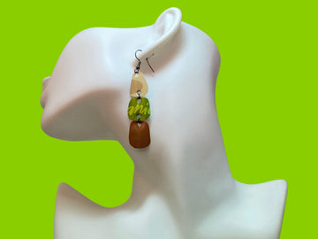 Earthy coloured, sand, green, gold earrings made from upcycled nespresso capsules on a white mannequin and green background