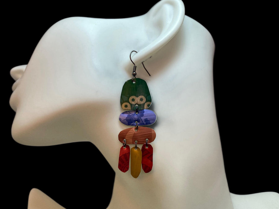 bright, colourful, green, blue, red, gold earrings made from recycled nespresso capsules on a white mannequin and grey background