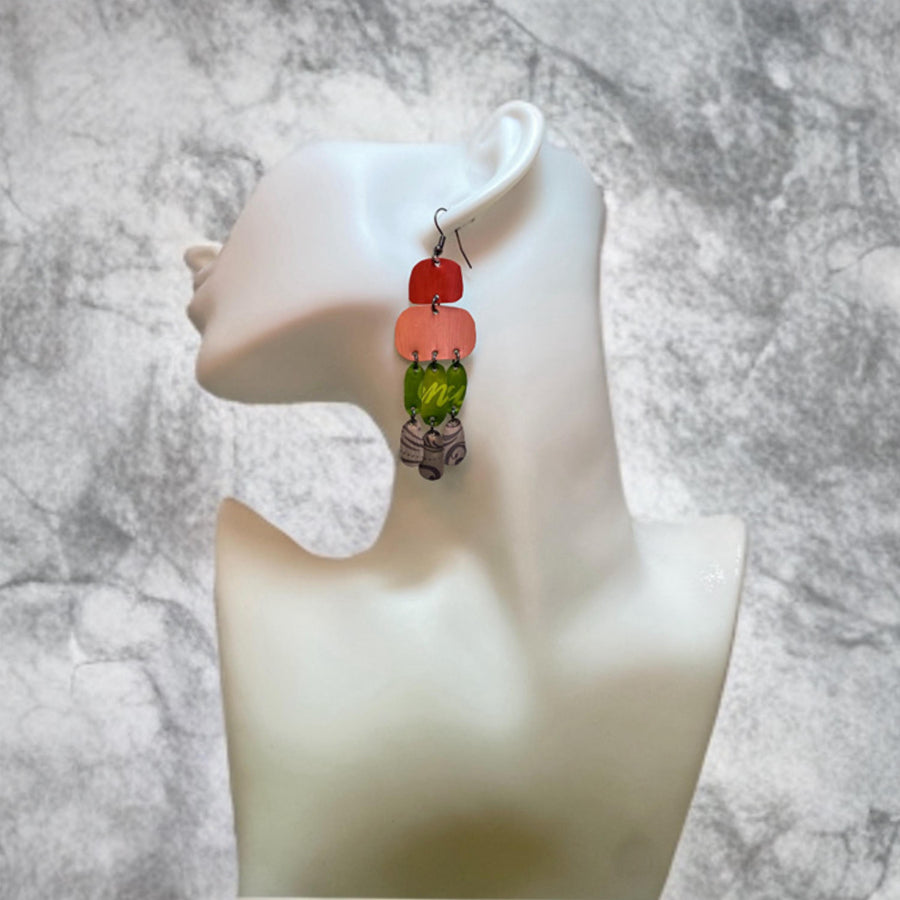 colourful oriental design earrings in red, peach, green and grey colour made from upcycled nespresso capsules on a white mannequin and concrete background