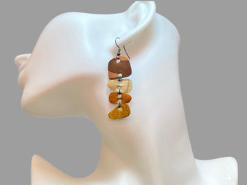 Earthy coloured, brown, sand mustard, gold earrings made from upcycled nespresso capsules on a white mannequin and grey background