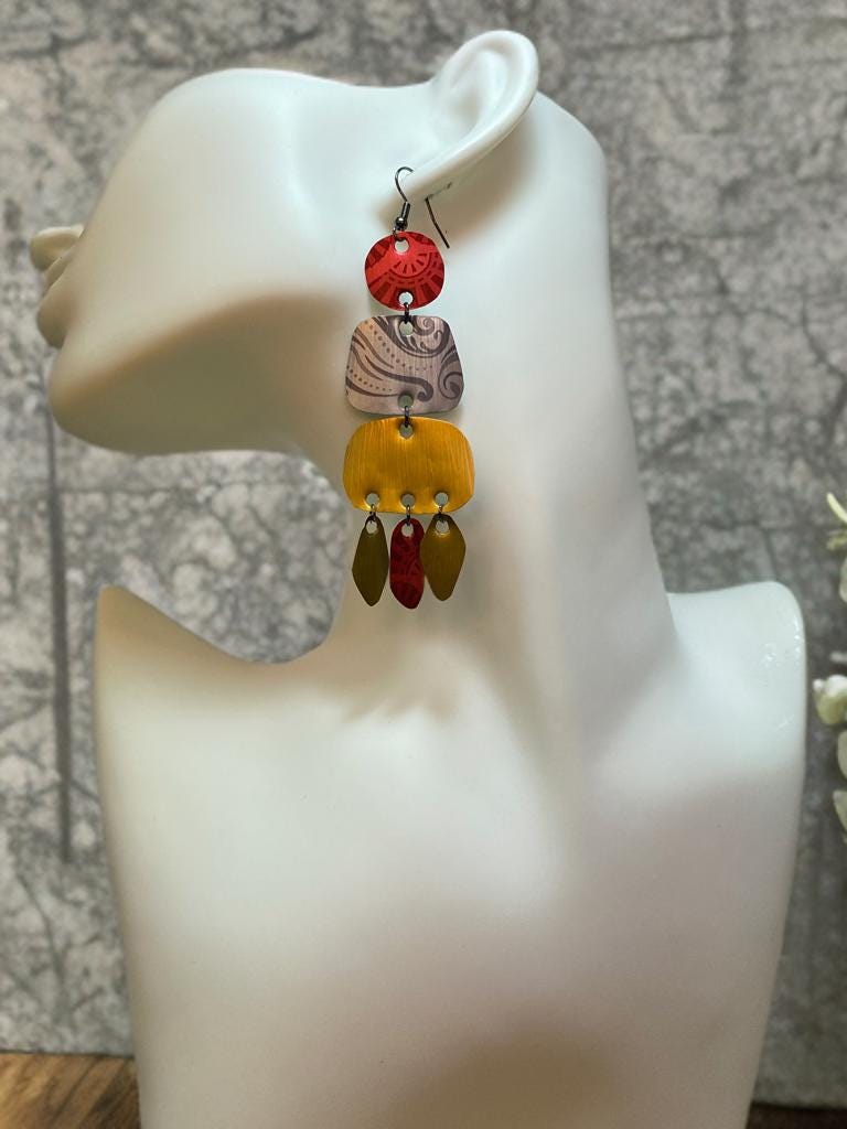 large, long, red, silver, golden earrings made from upcycled nespresso capsules on a white mannequin and concrete background