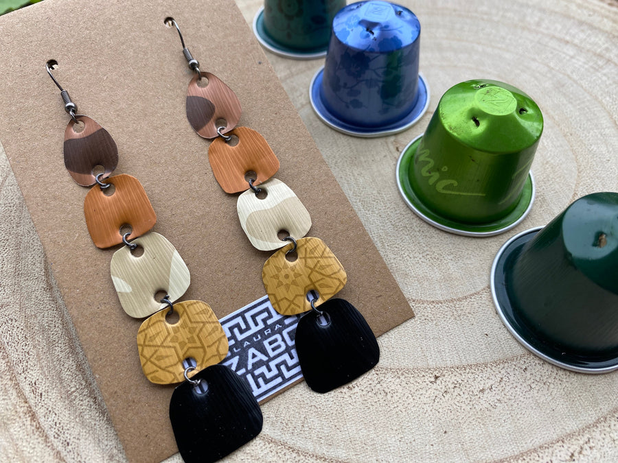 earthy coloured, brown black gold long earrings made from upcycled nespresso capsules on a wooden background, decorated with some whole nespresso capsules