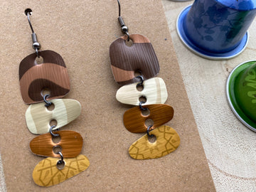 Earthy coloured, brown, sand mustard, gold earrings made from upcycled nespresso capsules on a wooden background with few whole nespresso pods