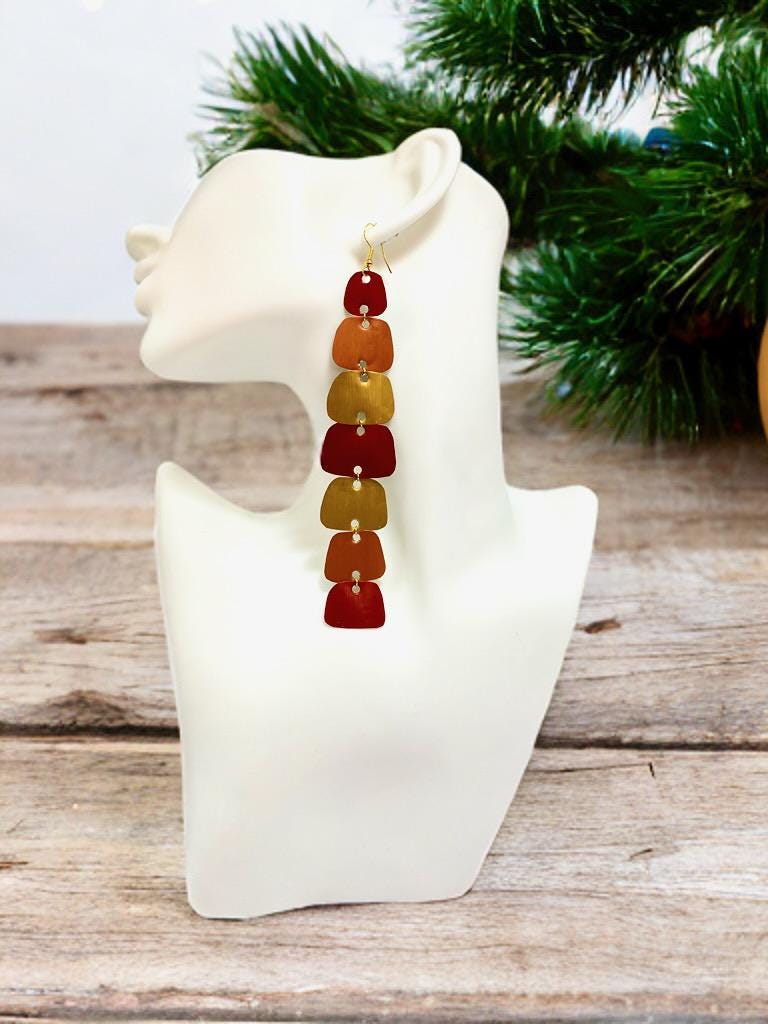 long, red, peach, gold earrings made from nespresso capsules on a white mannequin, pine tree and wooden background