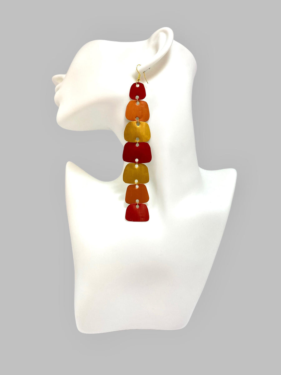 long, red, peach, gold earrings made from nespresso capsules on a white mannequin and grey background