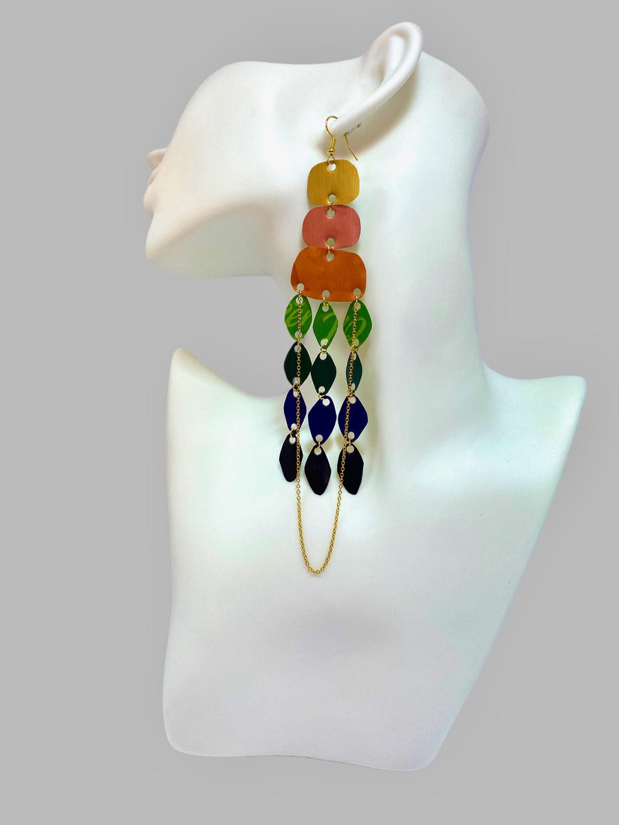 large, rainbow coloured chandelier earrings made from colourful Nespresso pods with a golden chain, on a white mannequin and grey background