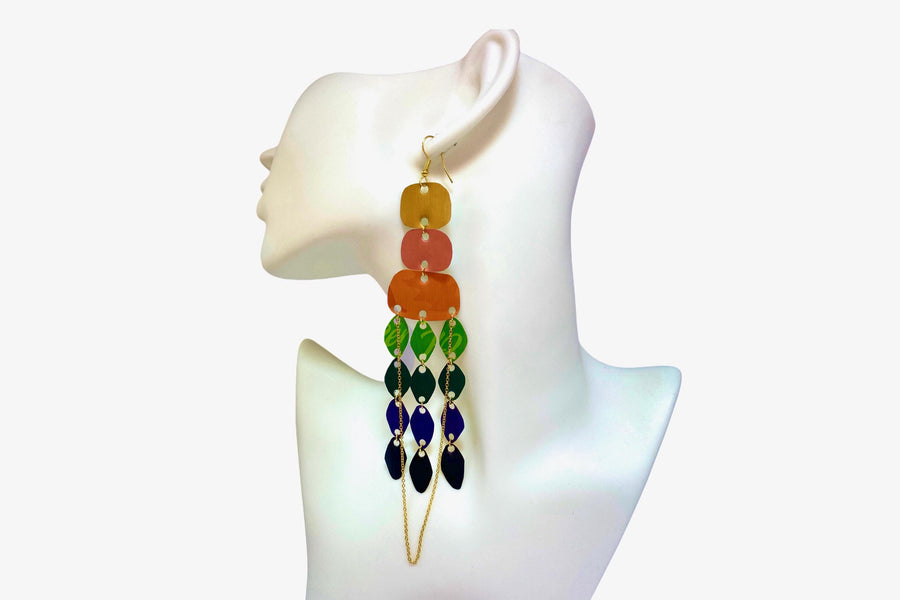 large, rainbow coloured chandelier earrings made from colourful Nespresso pods with a golden chain, on a white mannequin and white background