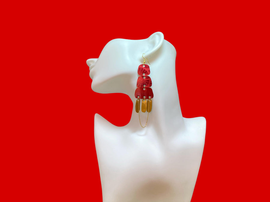 Golden red large earrings made from upcycled nespresso capsules on a white earrings display and red background