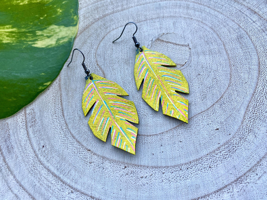 yellow coloured upcycled bicycle inner tube, tyre rubber earrings on a wooden background and a green  leaf