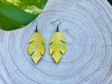 yellow coloured upcycled bicycle inner tube, tyre rubber earrings on a wooden background and a green  leaf