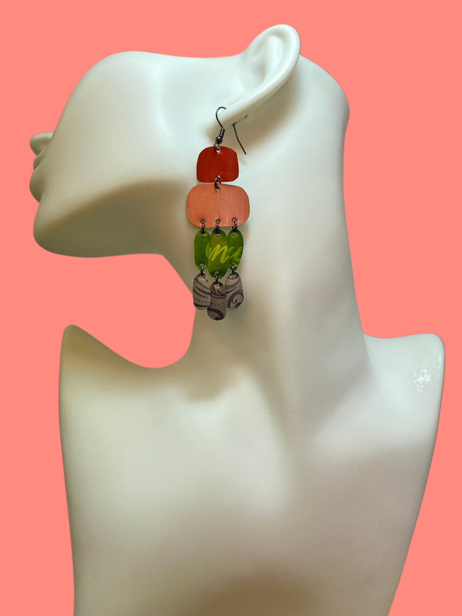 colourful oriental design earrings in red, peach, green and grey colour made from upcycled nespresso capsules on a white mannequin and peach background