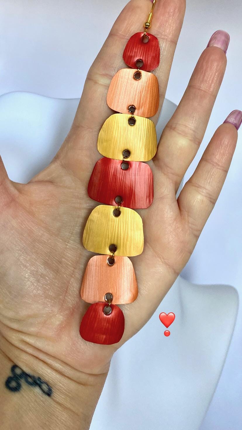 long, red, peach, gold earrings made from nespresso capsules in a hand and white background