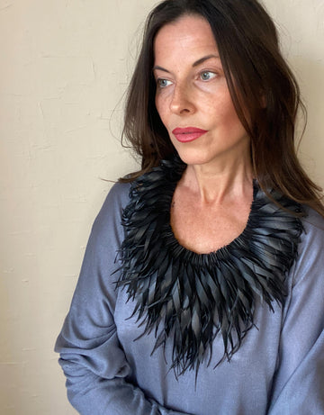 model wears large, quirky black, curly tassel necklace made from upcycled bicycle inner tube