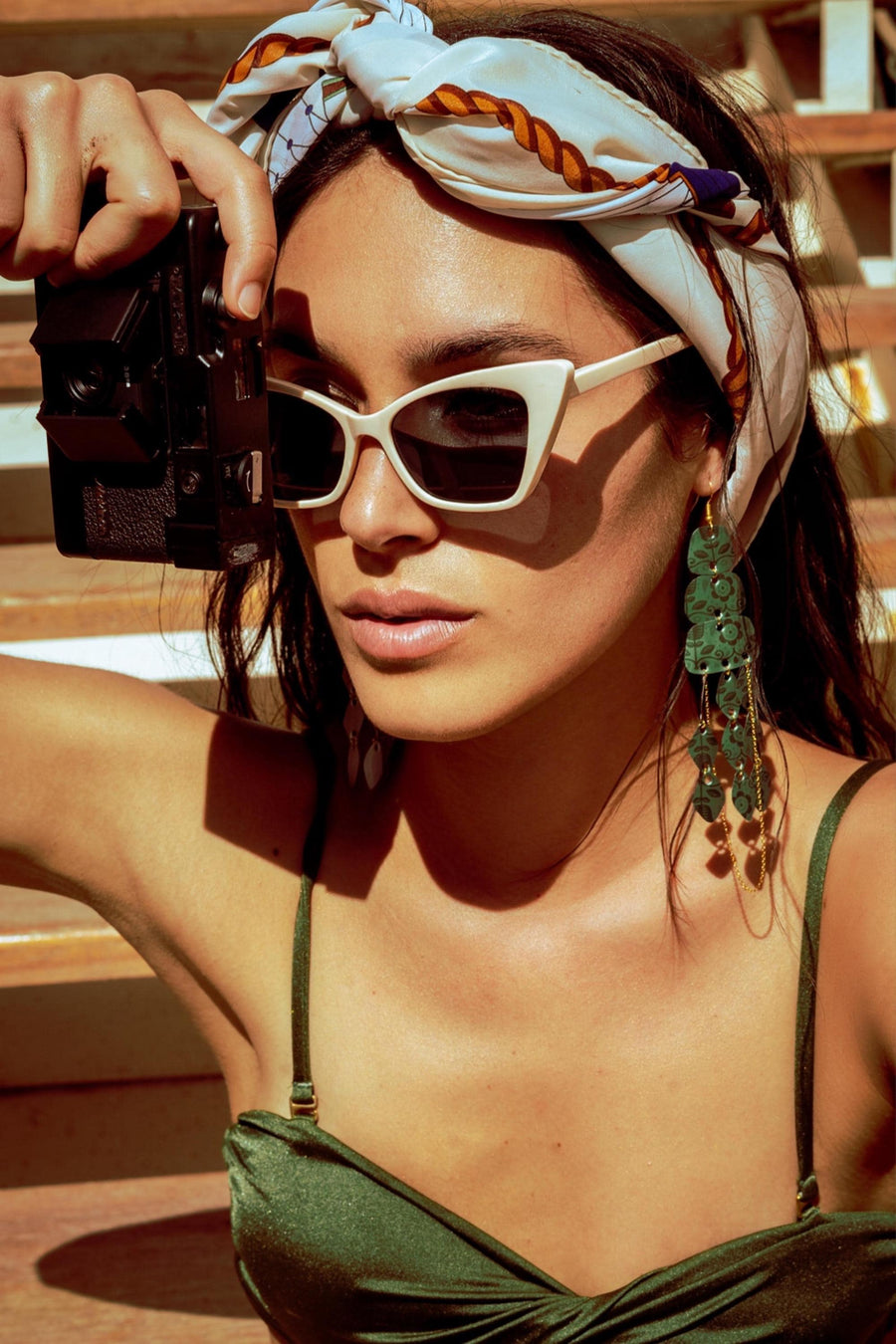 model wears dark green long chandelier earrings made from upcycled nespresso capsules in a bikini and holding a photo camera