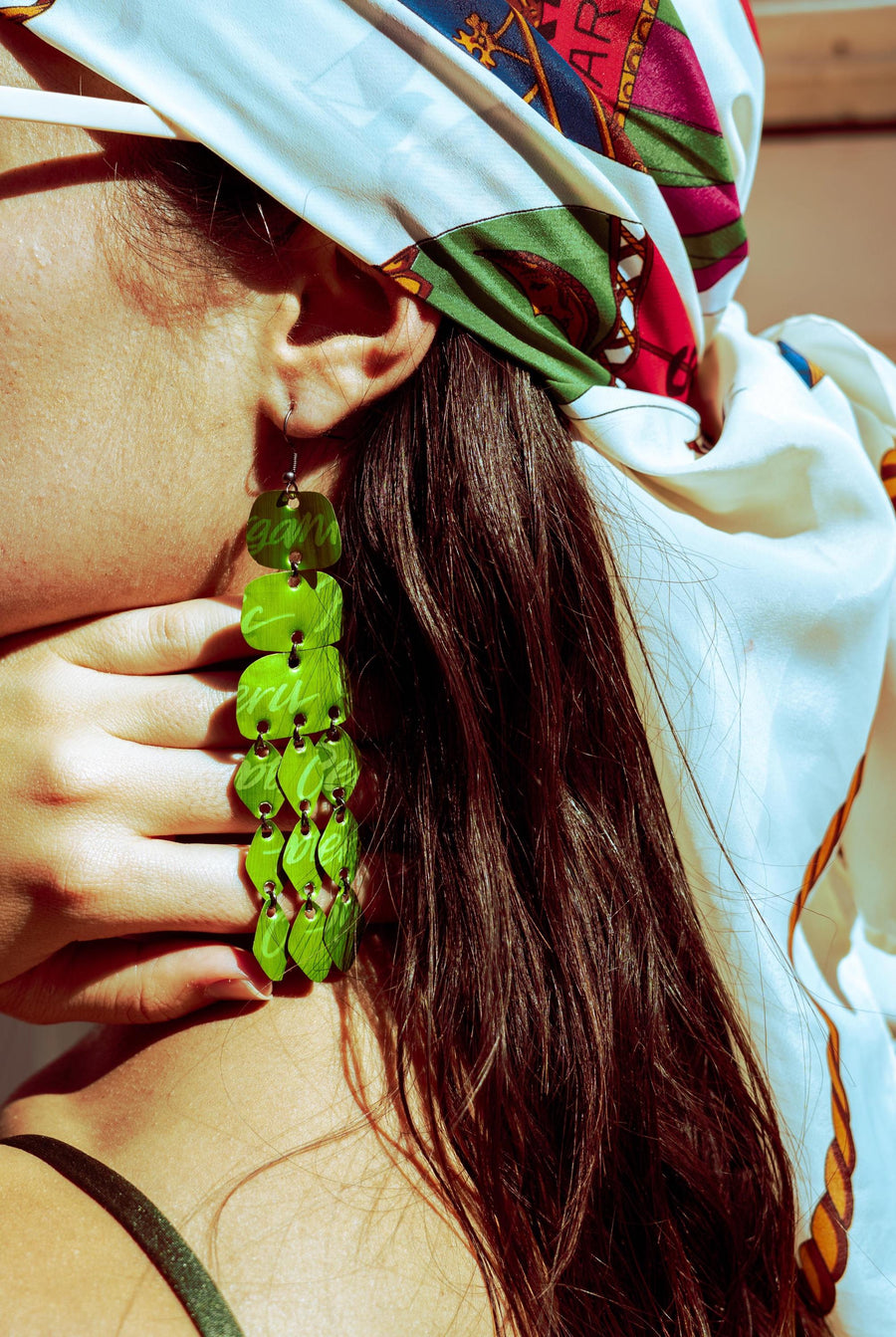 model wears  large, bold, bright green coloured chandelier earrings made from nespresso capsules in a bikini and beach environment