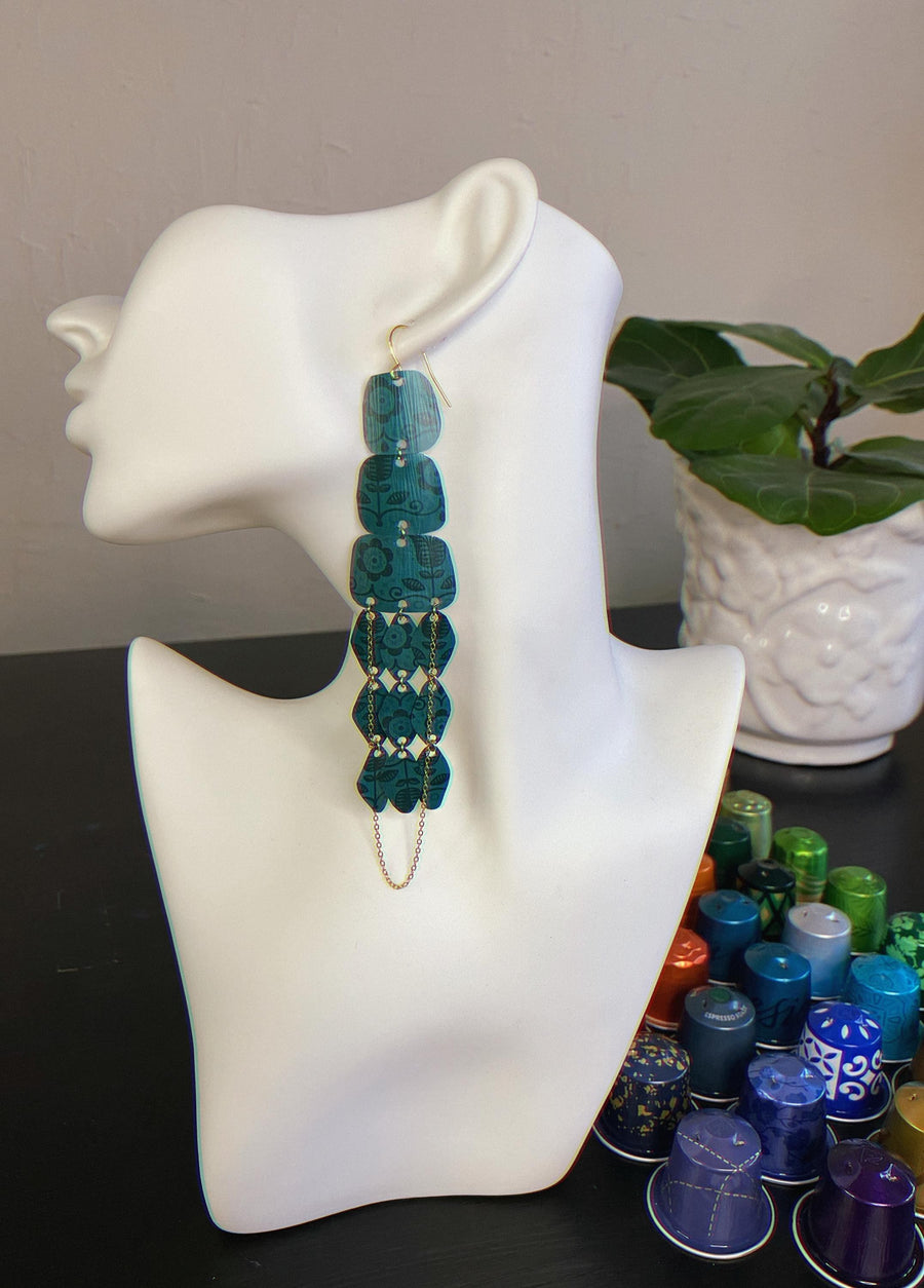 dark green long chandelier earrings made from upcycled nespresso capsules on a white mannequin displayed on a table with nespresso pods