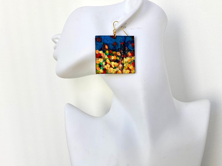 handpainted, square shape earrings, with blue, yellow, gold, red hues, made from upcycled bicycle inner tube and cork on a white head mannequin