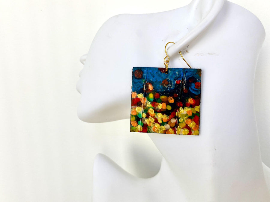 handpainted, square shape earrings, with blue, yellow, gold, red hues, made from upcycled bicycle inner tube and cork on a white head mannequin