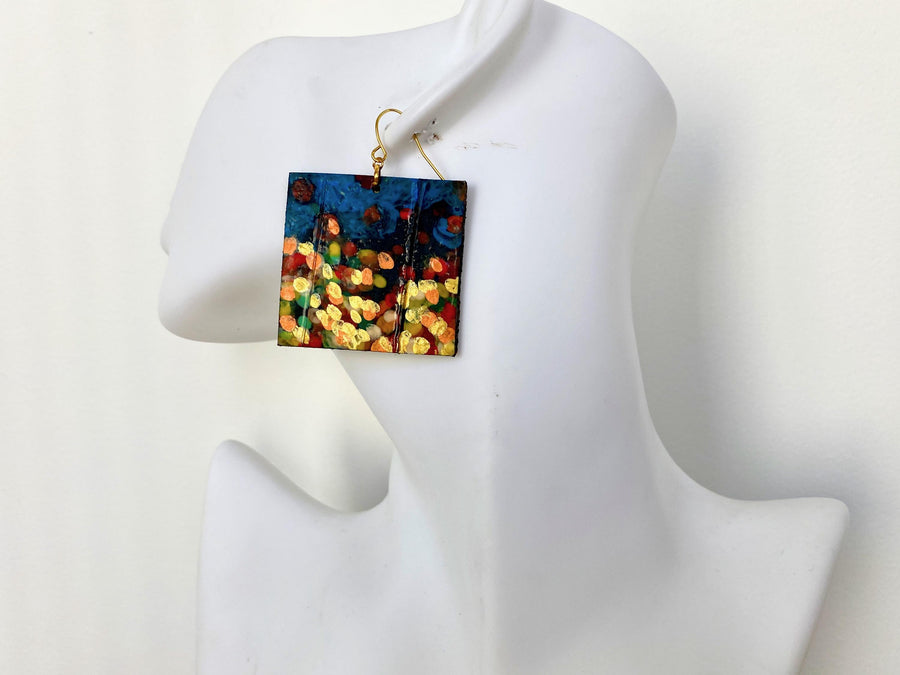 handpainted, square shape earrings, with blue, yellow, gold, red hues, made from upcycled bicycle inner tube and cork on a white head mannequin