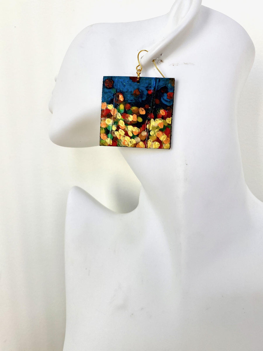 handpainted, square shape earrings, with blue, yellow, gold, red hues, made from upcycled bicycle inner tube and cork on a white head mannequin