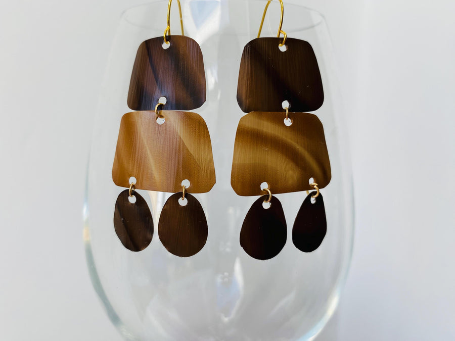 pair of brown earrings in oriental design made from upcycled nespresso capsules on a transparent wine glass
