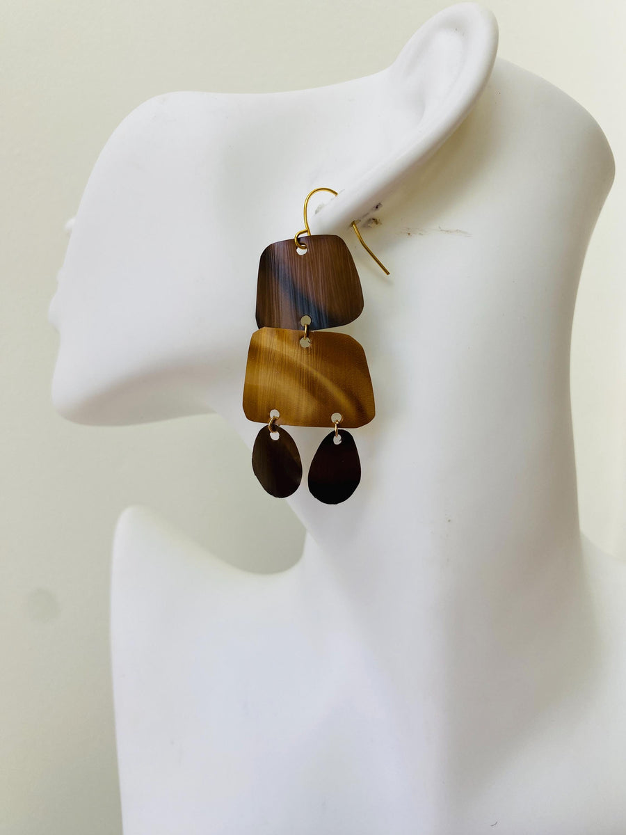 pair of brown earrings in oriental design made from upcycled nespresso capsules on a transparent wine glass