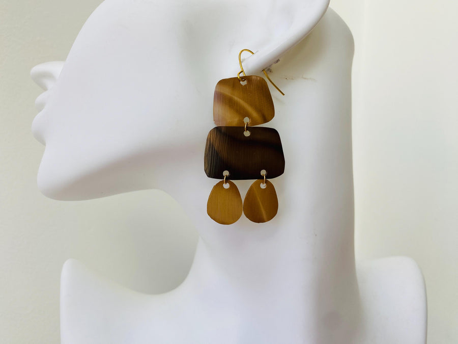 pair of brown earrings in oriental design made from upcycled nespresso capsules on a transparent wine glass