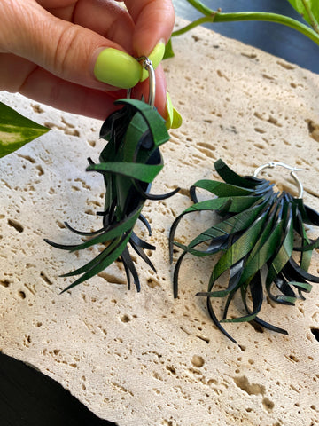 Pair of green, curly statement earrings made from upcycled bicycle inner tube rubber by laura zabo on a marble display