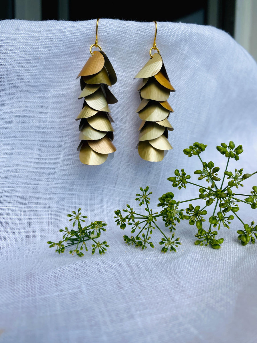 pair of creme-gold coloured, cascading earrings made from upcycled nespresso pod aluminium, on a white linen background and a little green flower