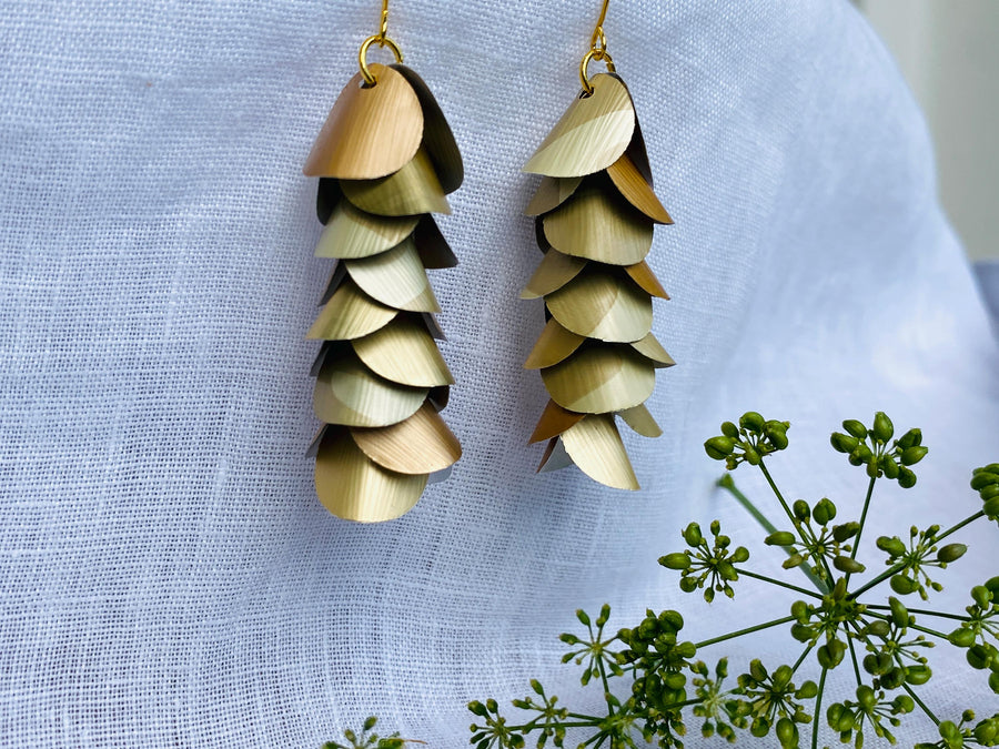 pair of creme-gold coloured, cascading earrings made from upcycled nespresso pod aluminium, on a white linen background and a little green flower