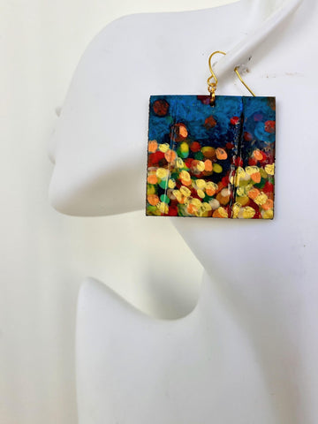 handpainted, square shape earrings, with blue, yellow, gold, red hues, made from upcycled bicycle inner tube and cork on a white head mannequin