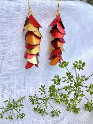 red orange gold cascade earrings made from upcycled nespresso capsule aluminium on a white linen background and green flower