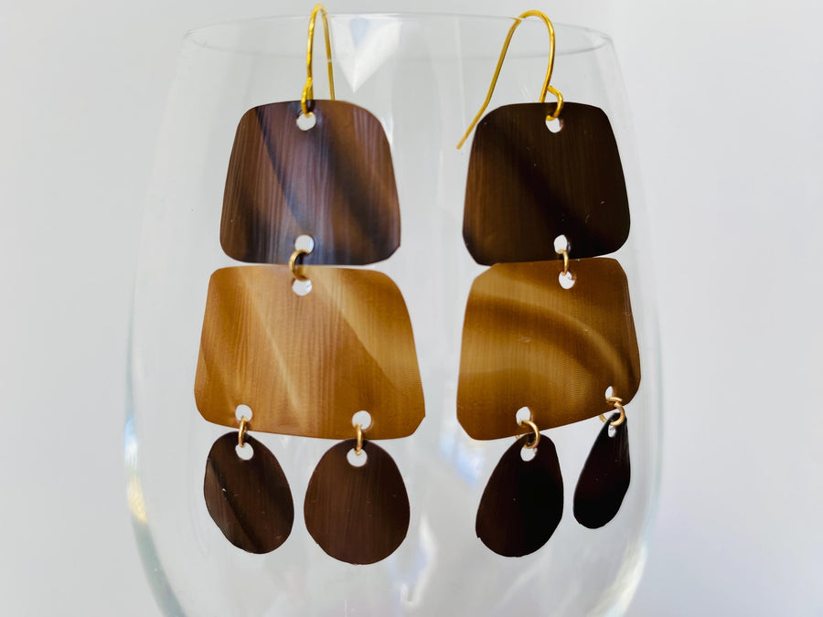 pair of brown earrings in oriental design made from upcycled nespresso capsules on a transparent wine glass