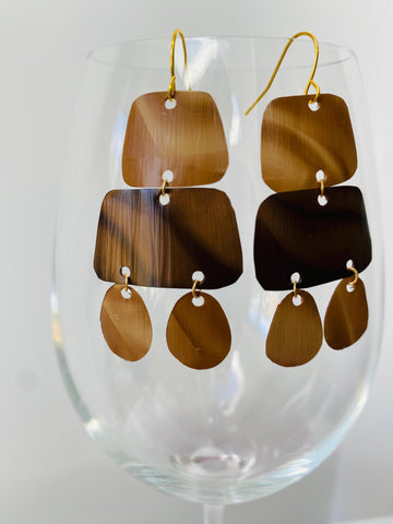 pair of brown earrings in oriental design made from upcycled nespresso capsules on a transparent wine glass