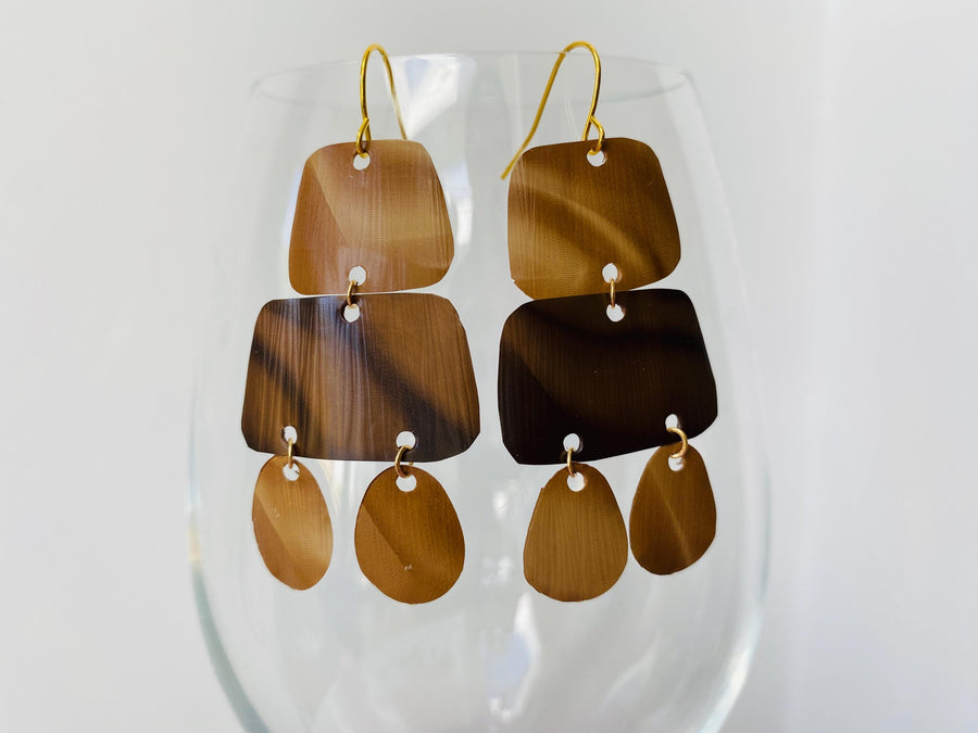 pair of brown earrings in oriental design made from upcycled nespresso capsules on a transparent wine glass