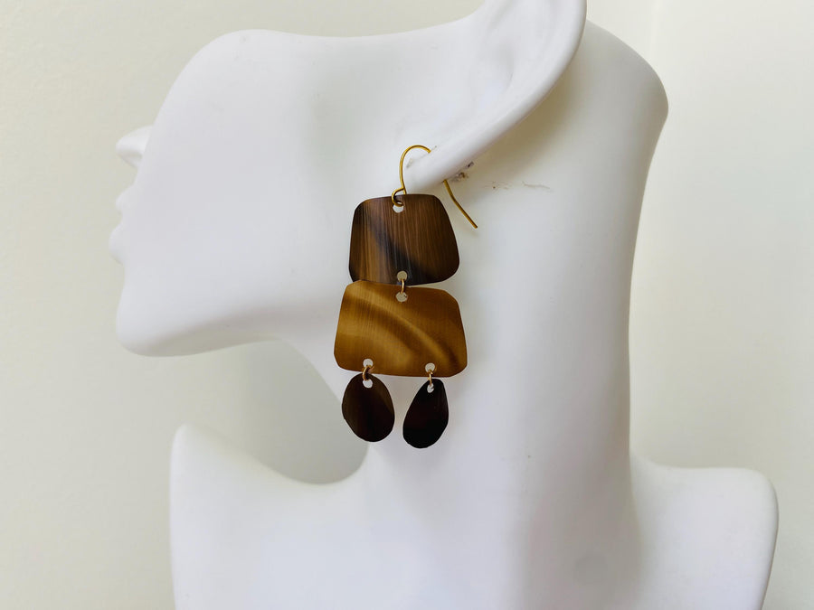 pair of brown earrings in oriental design made from upcycled nespresso capsules on a transparent wine glass