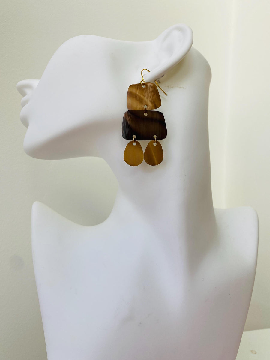pair of brown earrings in oriental design made from upcycled nespresso capsules on a transparent wine glass