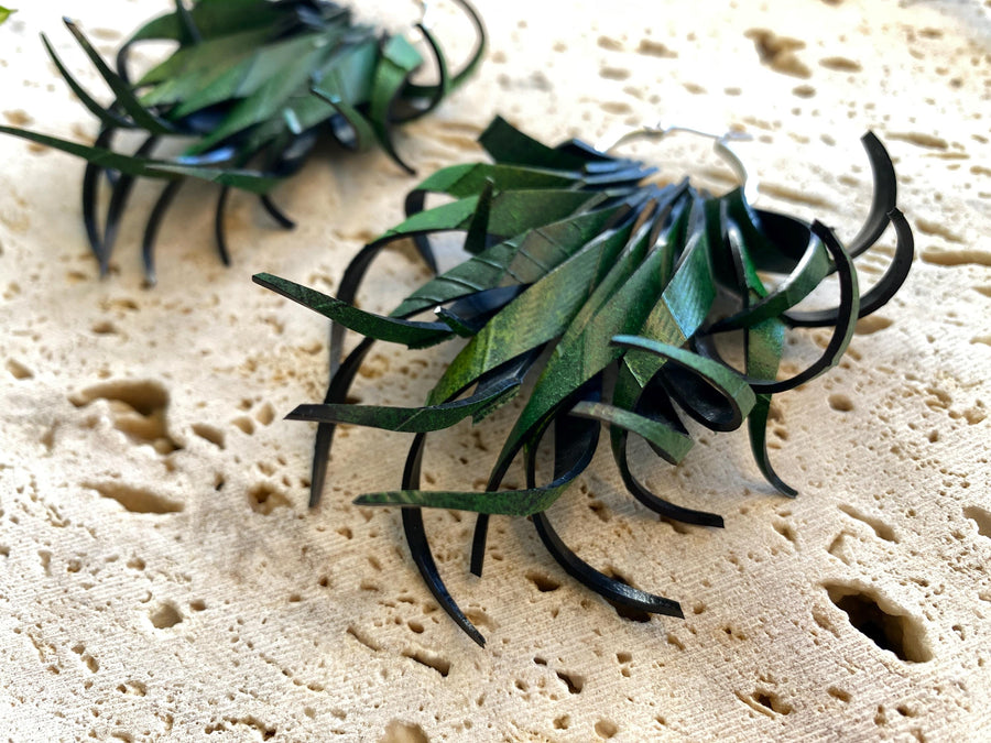 Pair of green, curly statement earrings made from upcycled bicycle inner tube rubber by laura zabo on a marble display