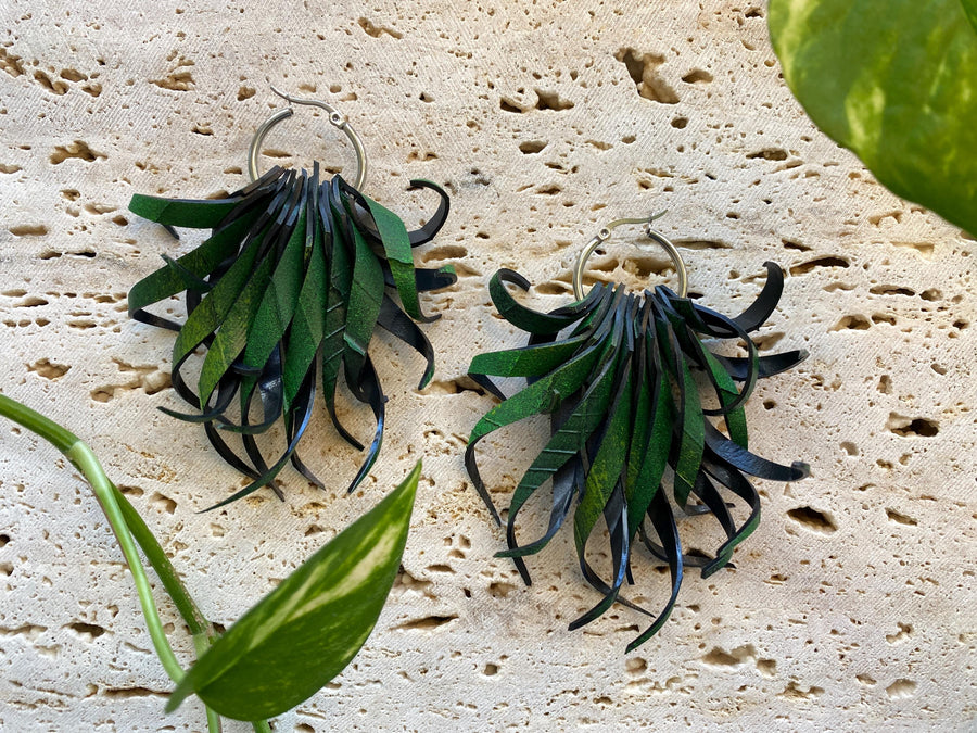 Pair of green, curly statement earrings made from upcycled bicycle inner tube rubber by laura zabo on a marble display