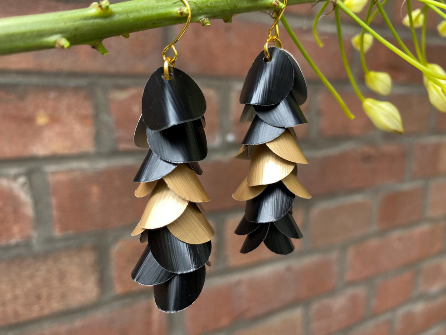 gold black cascade earrings made from upcycled nespresso capsules aluminium on a brick wall background