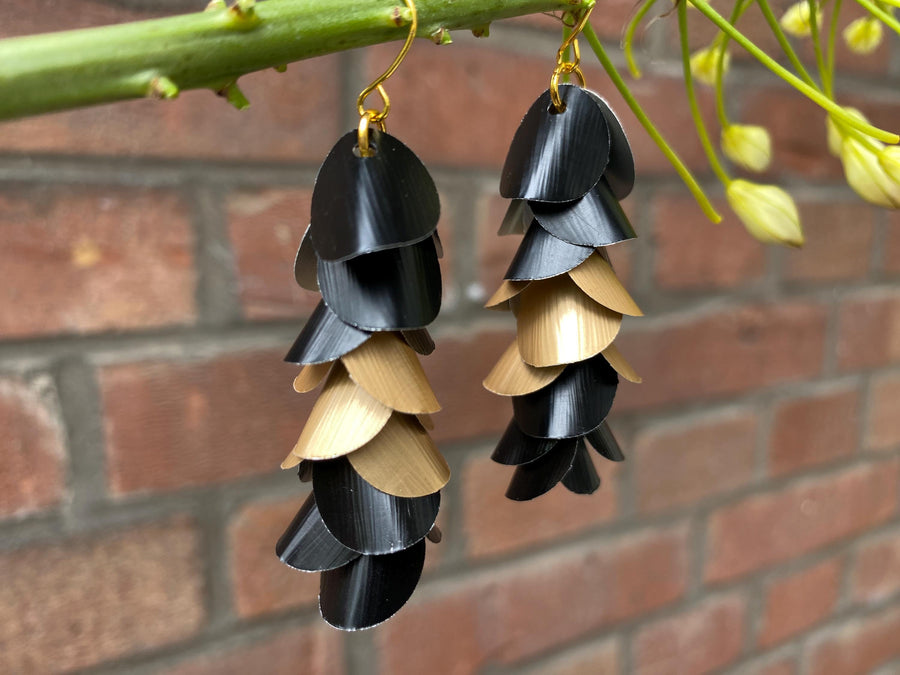 gold black cascade earrings made from upcycled nespresso capsules aluminium on a brick wall background