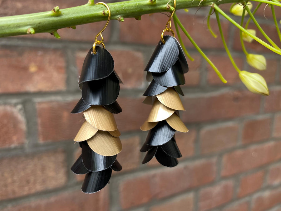 gold black cascade earrings made from upcycled nespresso capsules aluminium on a brick wall background
