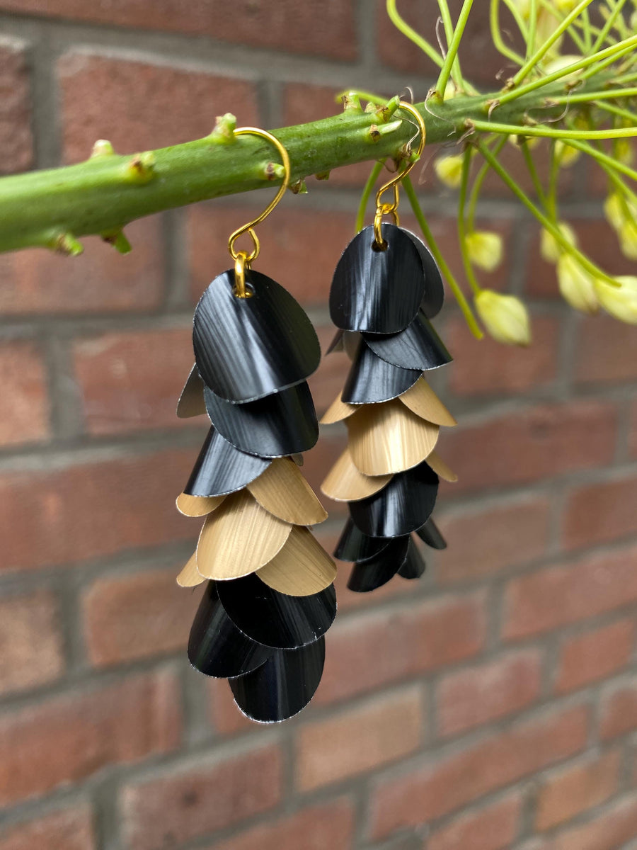 gold black cascade earrings made from upcycled nespresso capsules aluminium on a brick wall background