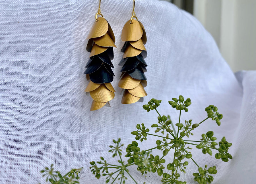 gold-black cascading earrings made from upcycled nespresso capsule aluminium on a white linen background and green flower