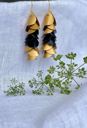 gold-black cascading earrings made from upcycled nespresso capsule aluminium on a white linen background and green flower