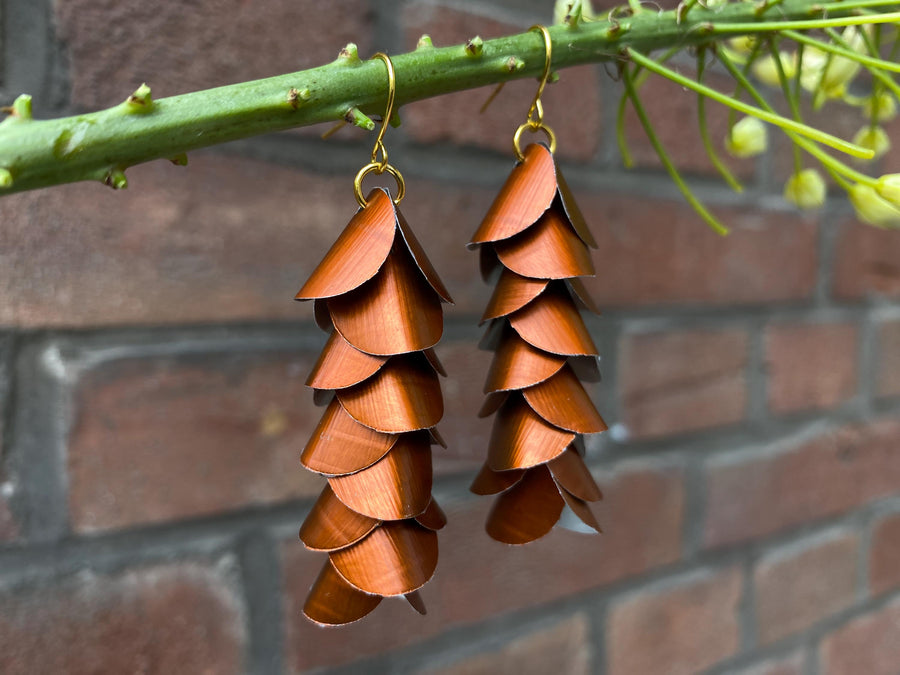 copper coloured cascade earrings made from upcycled nespresso capsule aluminium on a brick wall background