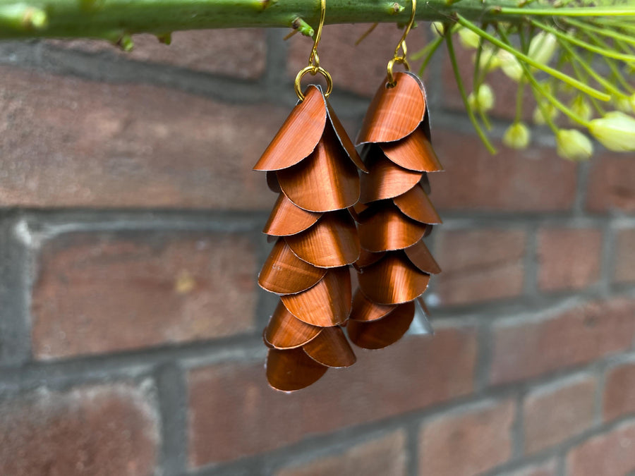 copper coloured cascade earrings made from upcycled nespresso capsule aluminium on a brick wall background